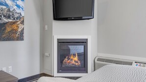 A modern room with a fireplace, a mounted television, and a painting on the wall. - Northwinds | Deluxe King (Canmore)
