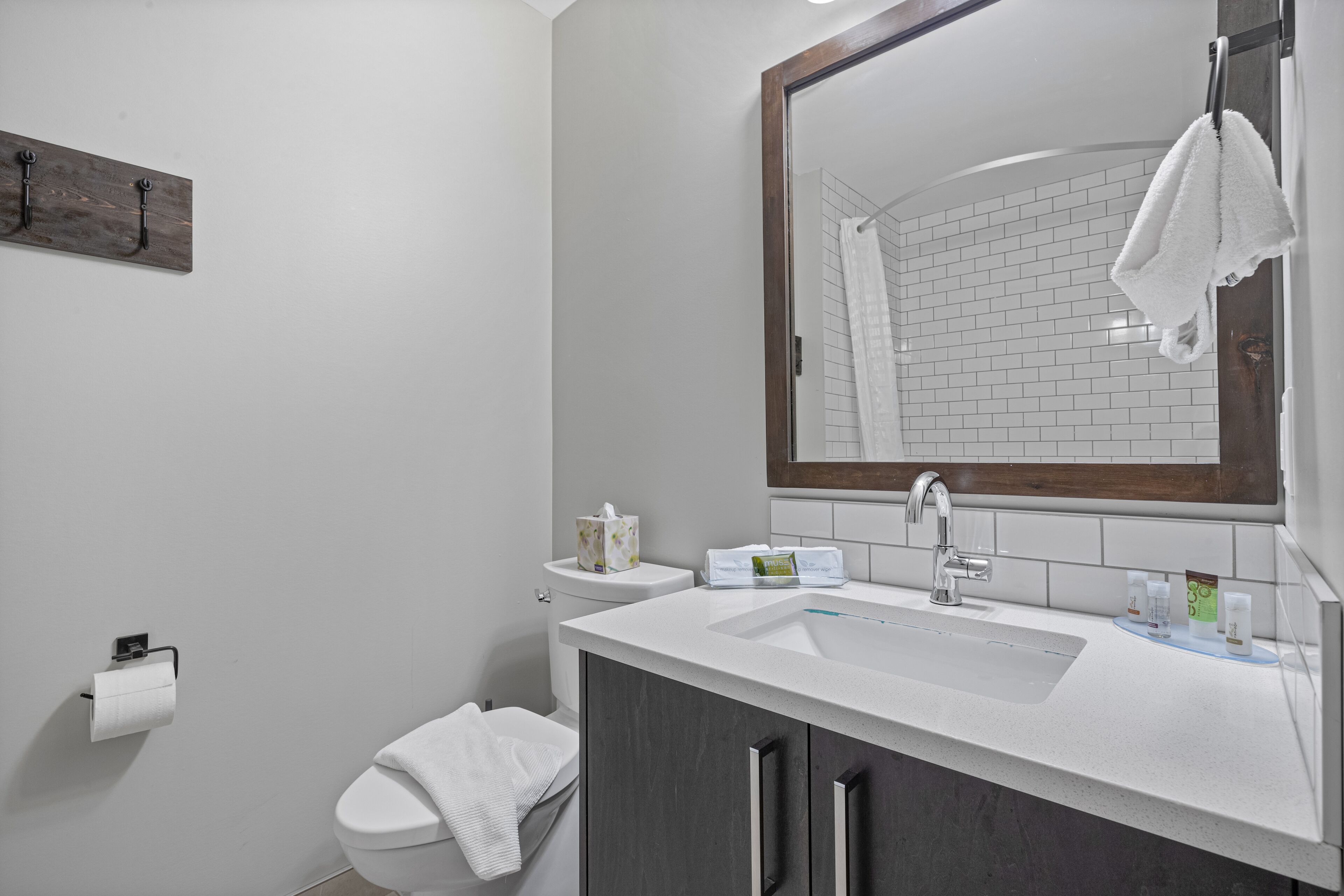 A modern bathroom with a white sink, a mirror, a towel hanging on the wall, and a toilet.