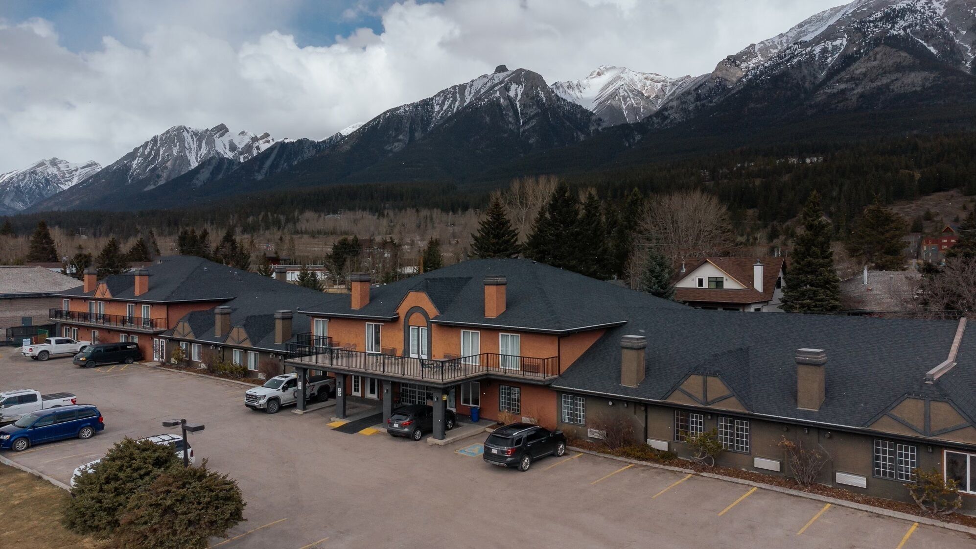 A hotel with a parking lot, a covered outdoor area, and a view of snow-capped mountains.