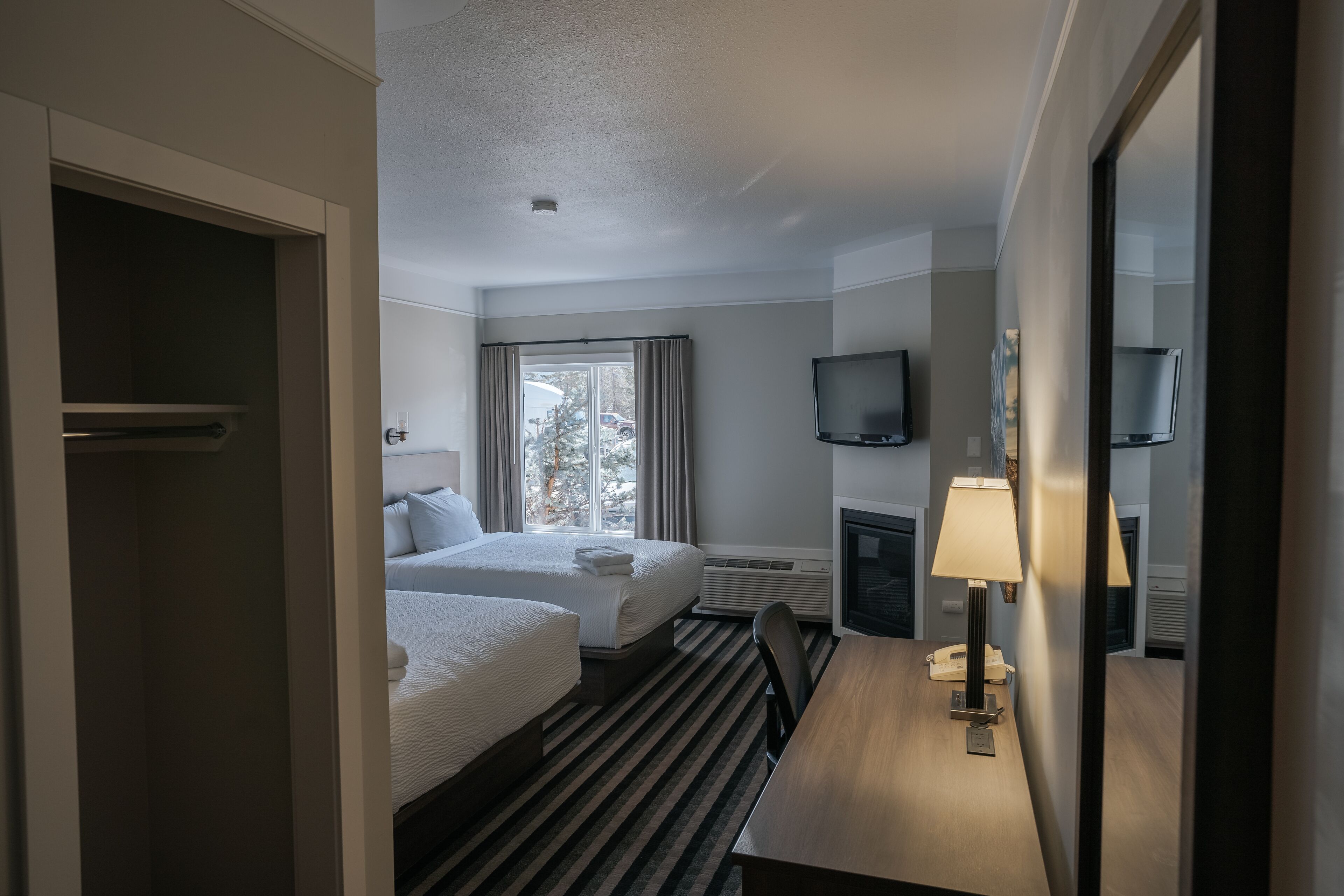 A hotel room with two beds, a desk, a TV, and a window with curtains.
