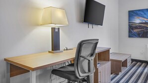 Une chambre d’hôtel avec un bureau en bois, un fauteuil de bureau noir, une lampe, un téléviseur à écran plat et un tableau au mur.