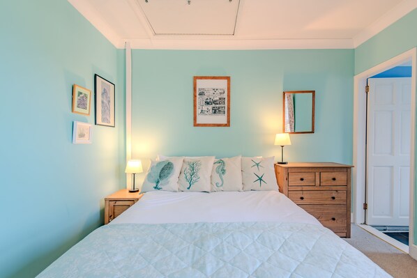 Un dormitorio con cama, dos mesitas de noche, cómoda y una puerta.