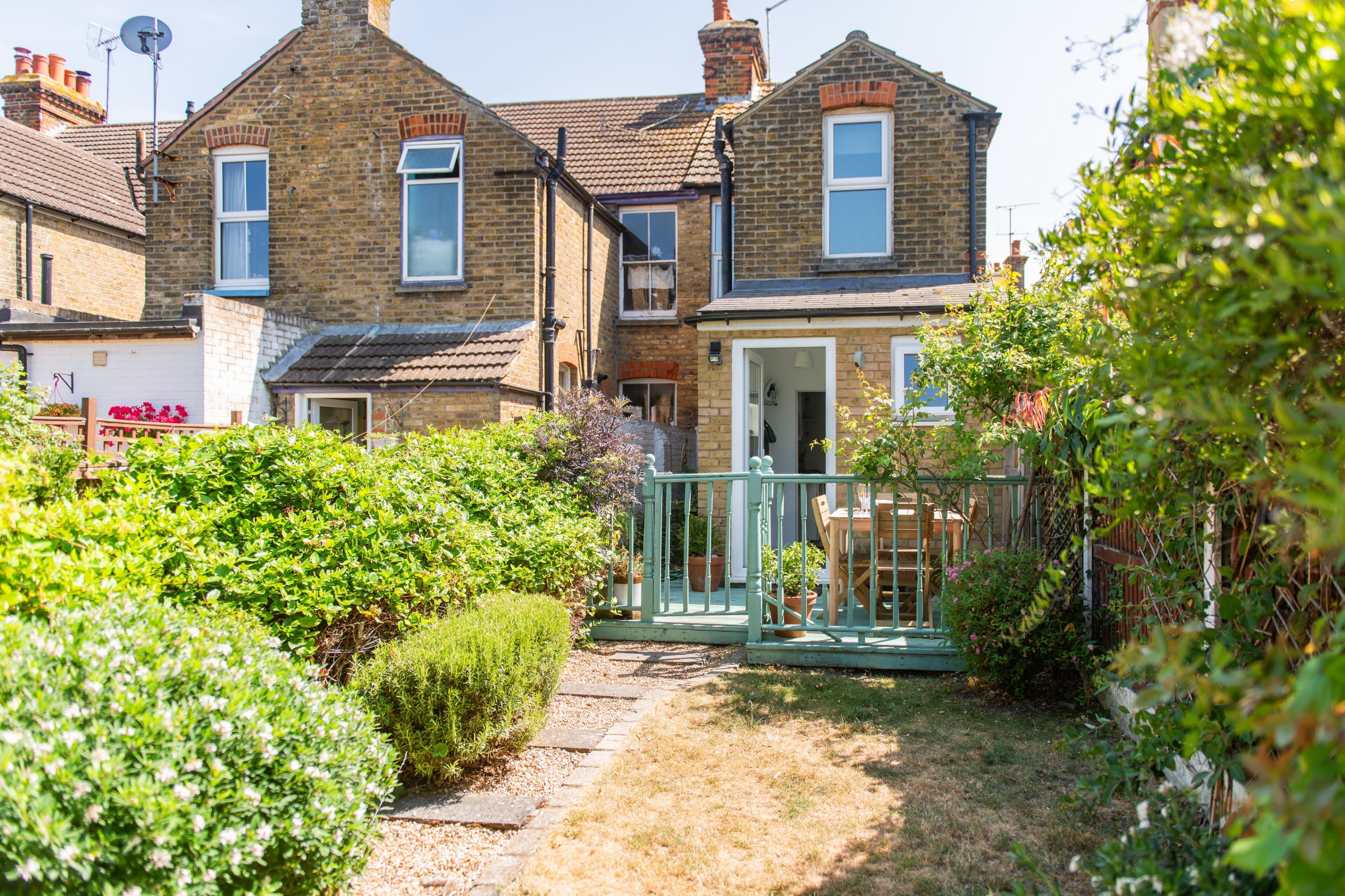 A residential property with a paved pathway leading to a front door, surrounded by greenery and a small garden.