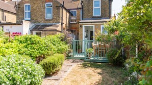 A residential property with a paved pathway leading to a front door, surrounded by greenery and a small garden.