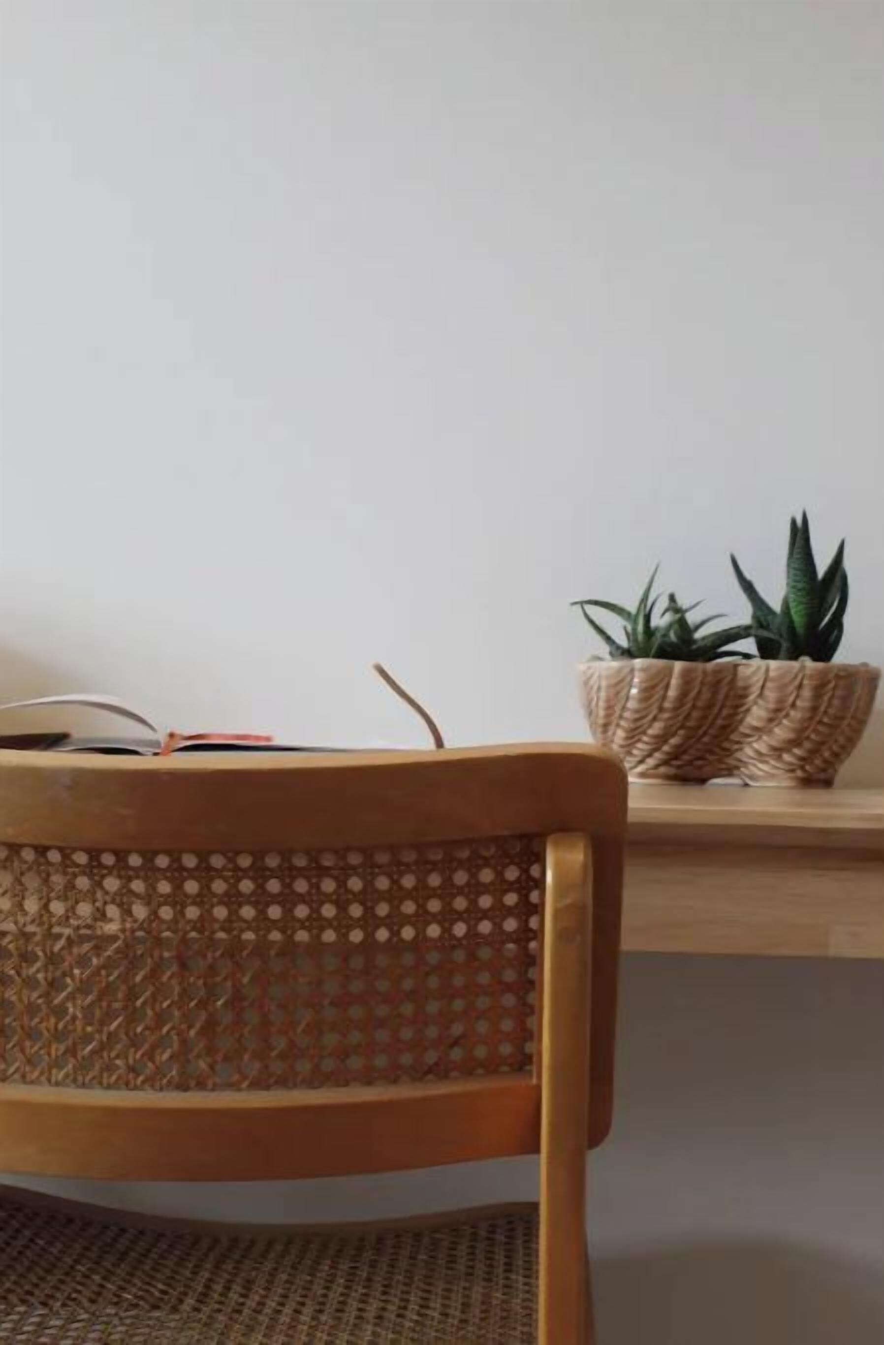 Una silla de madera con respaldo tejido, una mesa de madera y una cesta tejida que contiene una planta.