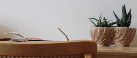 Una silla de madera con respaldo tejido, una mesa de madera y una cesta tejida que contiene una planta.