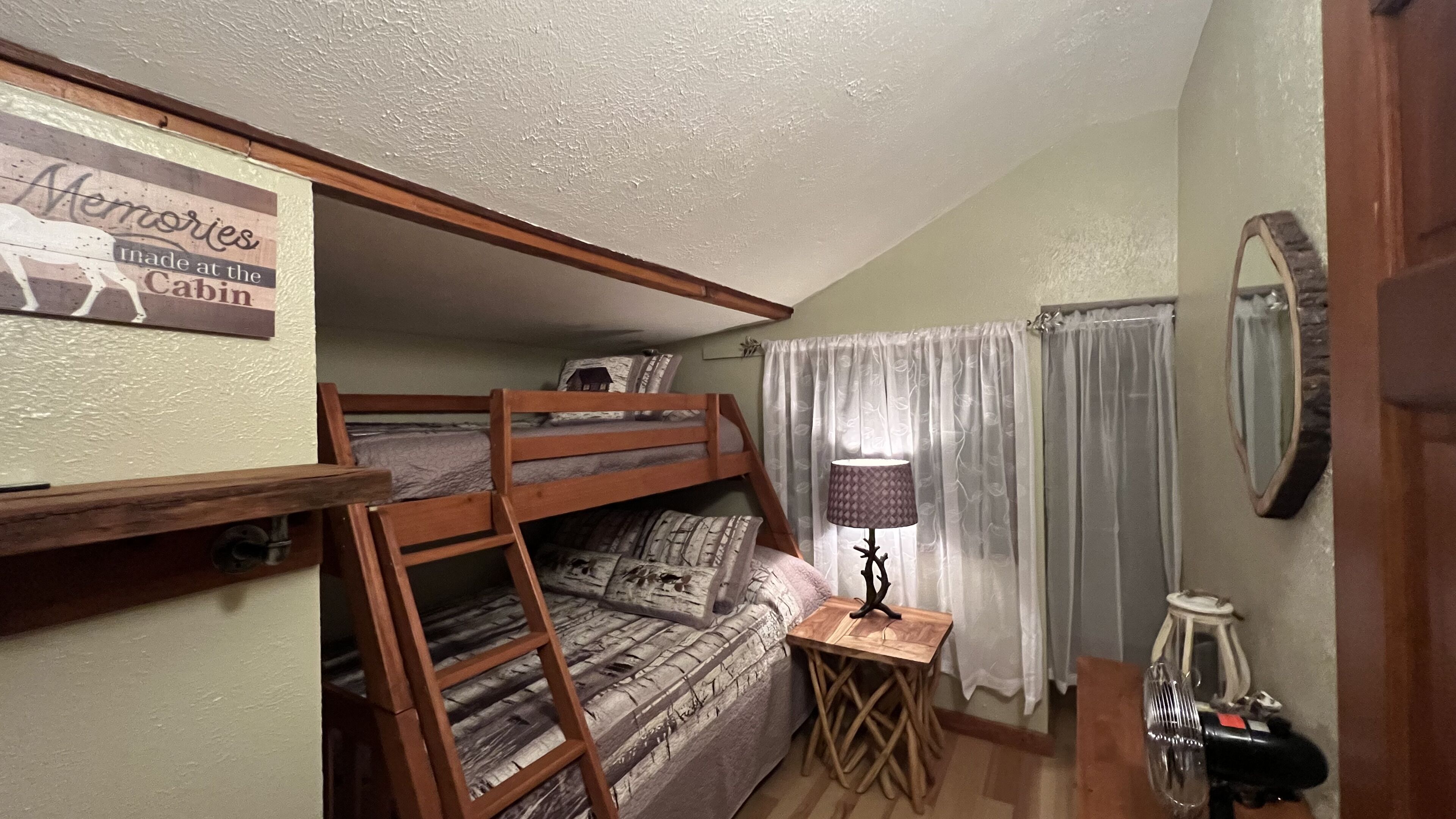 A bunk bed room with a ladder, a small table with a lamp, and a mirror on the wall.