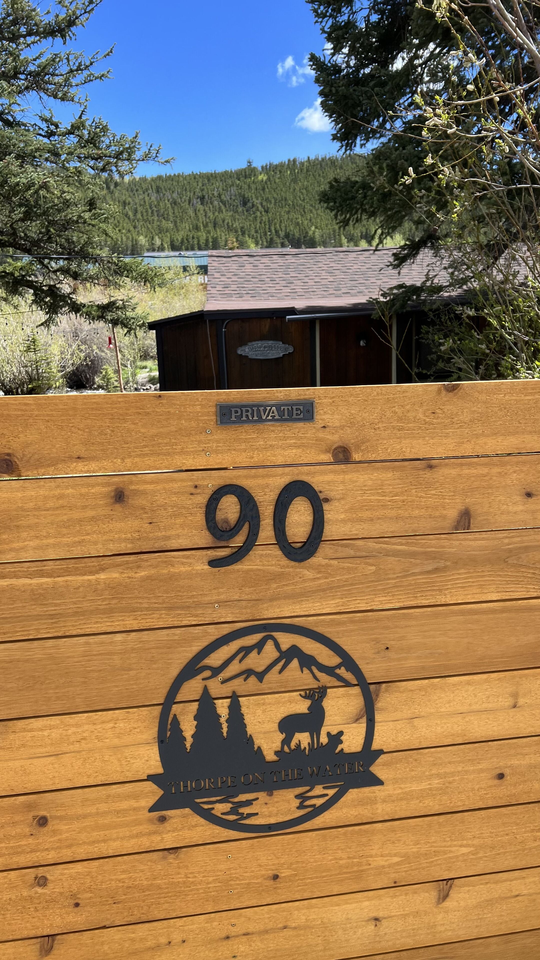 A wooden sign with the number 90 and a logo featuring a mountain, trees, and a deer.