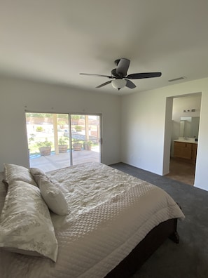 A bedroom with a bed, a ceiling fan, and a view of a patio with potted plants.