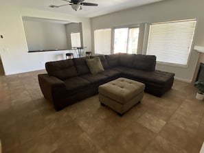 A living room with a sectional sofa, an ottoman, a ceiling fan, and a dining area with a table and chairs.