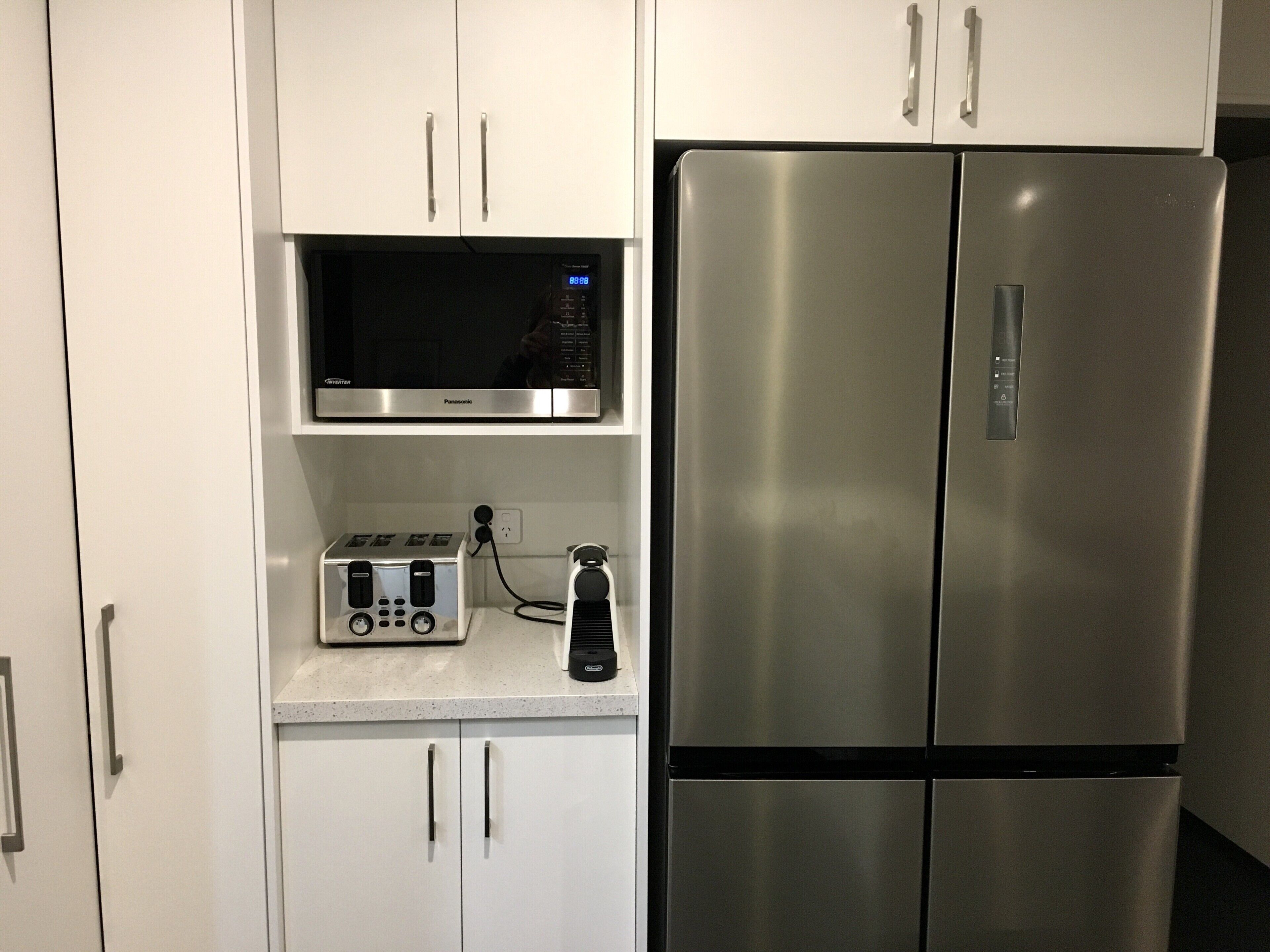 A kitchen with white cabinets, a stainless steel refrigerator, a microwave, and a toaster.