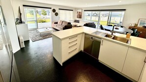Una cocina moderna con lavavajillas, un comedor con mesa y sillas, un sofá, y un amplio ventanal con vistas al exterior.