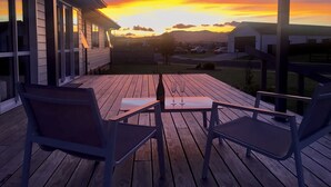 Una terraza de madera con dos sillas y una mesa, con vistas a una zona residencial al atardecer.