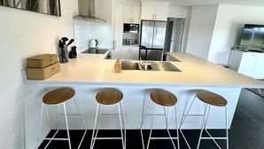 Una cocina moderna con una isla central, taburetes de bar, electrodomésticos de acero inoxidable y un televisor de pantalla plana.