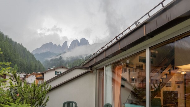 Une terrasse avec des chaises vertes et une table, une vue sur les montagnes et un bâtiment doté d’un escalier.