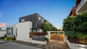 A modern building with a flat roof, a wooden fence, and a paved driveway. - StayCentral Northcote Townhouse With Study (Northcote)