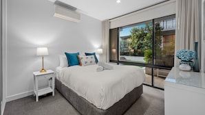 A modern bedroom with a large bed, white walls, and a view of a garden through a sliding glass door. - StayCentral Northcote Townhouse With Study (Northcote)