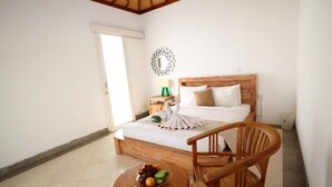 Un dormitorio con una cama, una silla de madera, una mesita con fruta y un espejo decorativo en la pared.