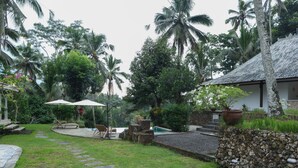 Un jardín tropical con un sendero de piedra, una piscina y un pabellón.