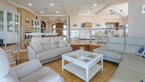 Een ruime woonkamer met een hoge plafond, een glazen salontafel en een open haard.