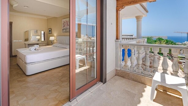 Een hotelkamer met een bed, een badkamer en een balkon met uitzicht op zee.