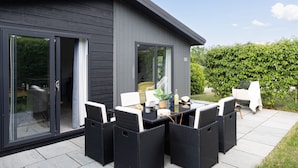 Een modern huis met een patio, voorzien van een glazen deur, een eettafel met stoelen en een kleine tuin.