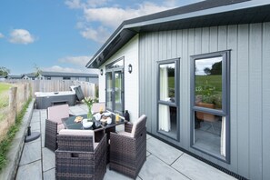 A patio with a table set for breakfast, wicker chairs, and a hot tub. - Daisy Lodge, 6 Roadford Lake Lodges (Lifton)