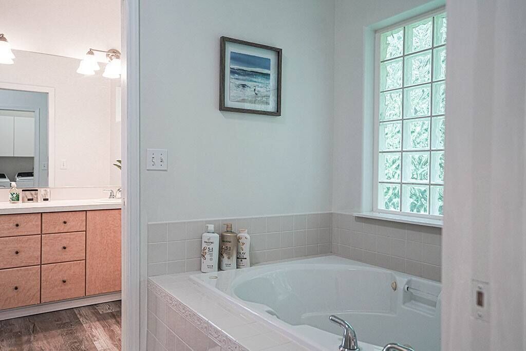 A bathroom with a bathtub, a sink, a mirror, and a window with frosted glass.