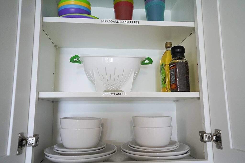 Ein Küchenschrank mit einem Sieb, Schüsseln und Kindergeschirr, Tassen und Tellern.