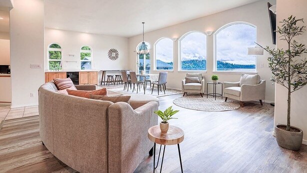 Ein großzügiger Wohnbereich mit Sofa, Sesseln und einem Esstisch. Große Fenster bieten Blick ins Freie.