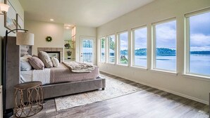 Ein geräumiges Schlafzimmer mit einem großen Bett, Seeblick und mehreren Fenstern.