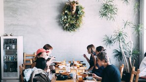 Un coin repas où un groupe de personnes est assis autour d’une table, un réfrigérateur rempli de boissons et une guirlande décorative accrochée au mur.