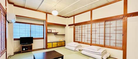 A traditional Japanese-style room with tatami flooring, a low wooden table, a television, and a sliding door with a grid pattern.