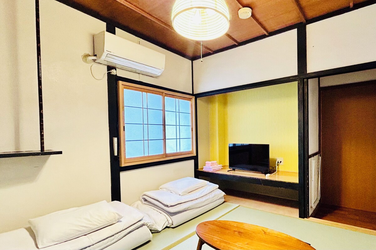 A traditional Japanese-style room with tatami flooring, a futon bed, a television, and a sliding door leading to another room.