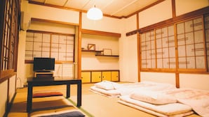 Una habitación japonesa tradicional con suelo de tatami, un televisor, una mesita baja y futones.