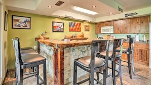 A kitchen with a bar area, wooden cabinets, a microwave, and a sign indicating a cold beer. - Kimberling City Monthly Stay w/ Lake Views! (Kimberling City)