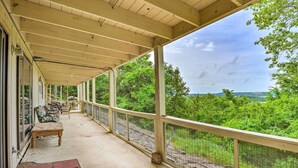 A covered outdoor area with a bench and chairs, a concrete floor, and a view of a lush green landscape. - Kimberling City Monthly Stay w/ Lake Views! (Kimberling City)