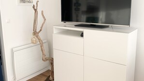 Un mueble blanco para televisor con televisor de pantalla plana, un cuadro en la pared y una rama decorativa de madera.