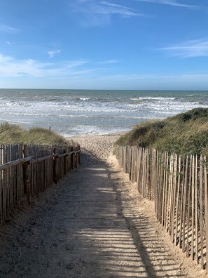 A sandy beach path leading to the ocean, flanked by wooden fences.