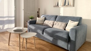 Una sala de estar moderna con un sofá gris, una mesita auxiliar blanca y una planta en maceta.