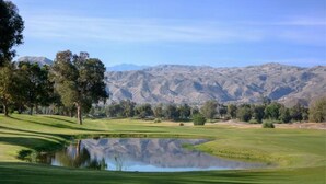 Un campo da golf con uno stagno, alberi e montagne sullo sfondo.