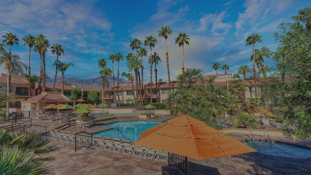 Un resort con piscina, palme e una zona salotto coperta.