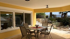 A covered patio with a table and chairs, large windows, and a view of the outdoors. - Twin Pines Home in Kounoupidiana Chania. (Κουνουπιδιανά)
