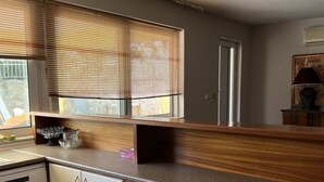 A modern kitchen with a wooden countertop, white cabinets, and a window with blinds. - Twin Pines Home in Kounoupidiana Chania. (Κουνουπιδιανά)