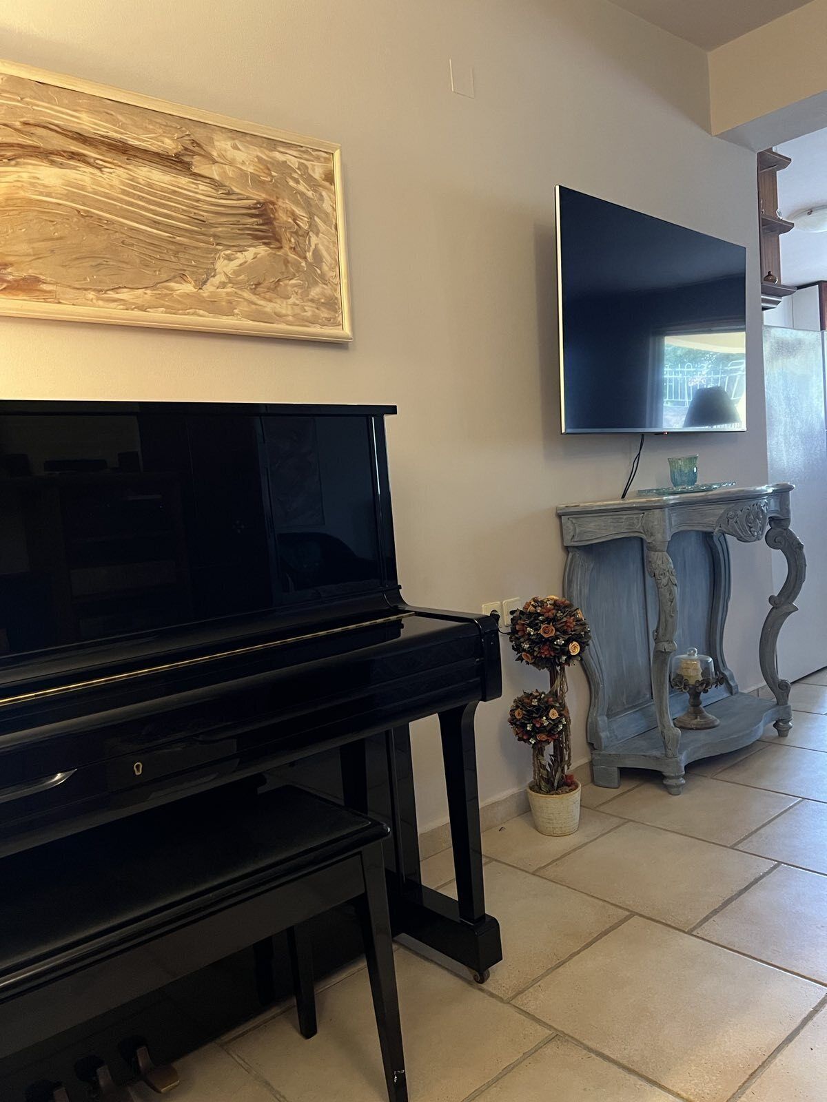 A living room with a black piano, a flat-screen TV, a decorative console table, and a painting on the wall.