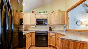 Une cuisine avec des meubles de rangement en bois, un réfrigérateur noir, un four à micro-ondes et une cuisinière.