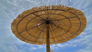 Ett strandparasoll med en randig flagga på en sandstrand.