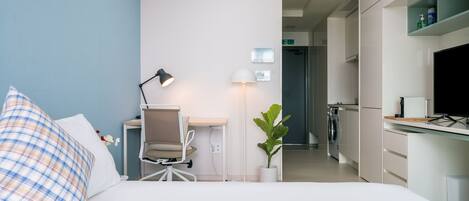Habitación de hotel con cama, escritorio, silla, lámpara, planta en maceta y televisor.
