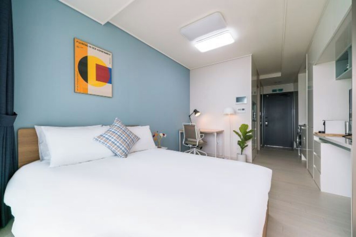 A modern hotel room with a large bed, a desk, and a kitchenette.