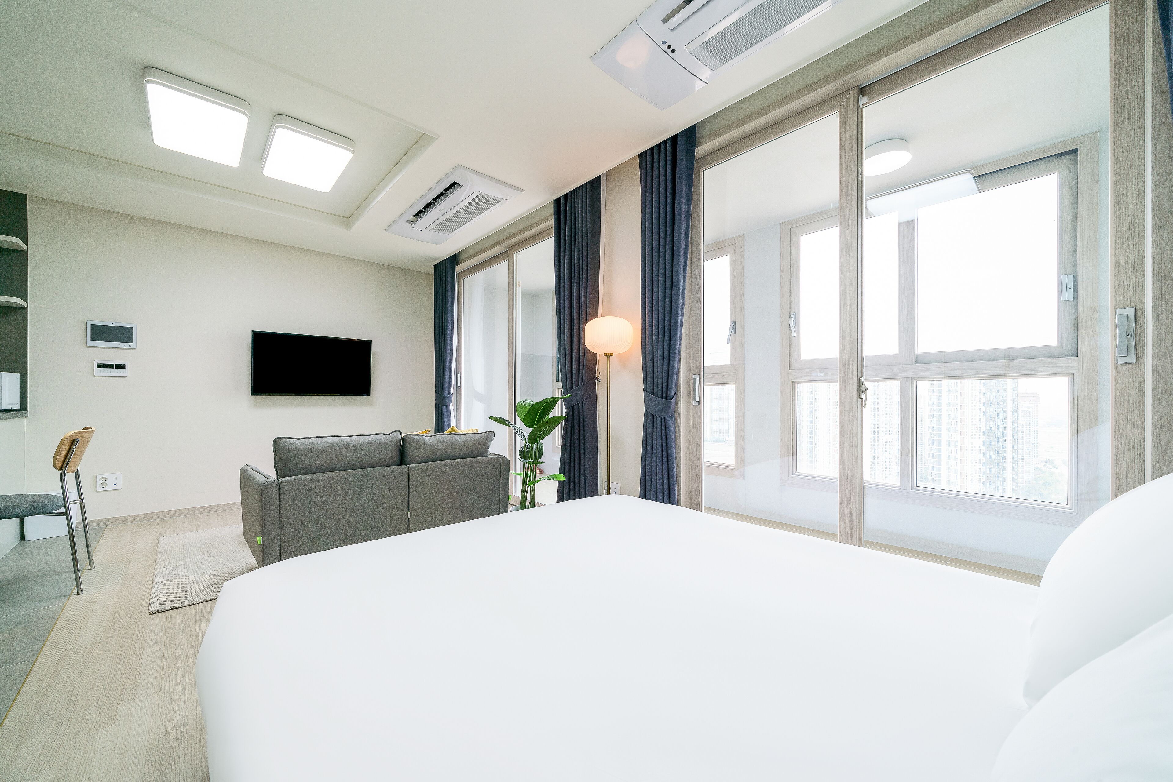 Une chambre d’hôtel moderne dotée d’un grand lit, d’un canapé, d’une télévision à écran plat et d’une grande fenêtre avec des rideaux.